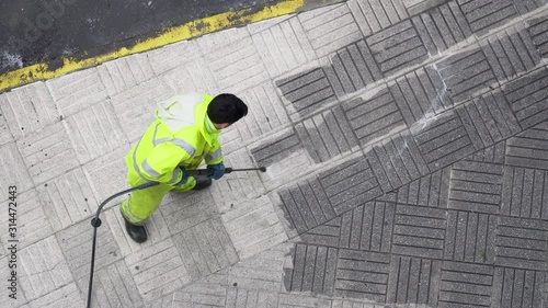 Top view of a Worker cleaning the street sidewalk with high pressure water jet. Public maintenance concept