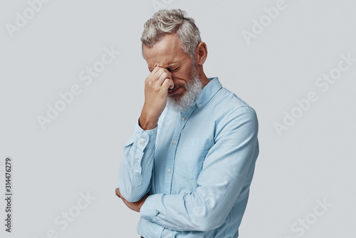 Tired mature man suffering from headache while standing against grey background