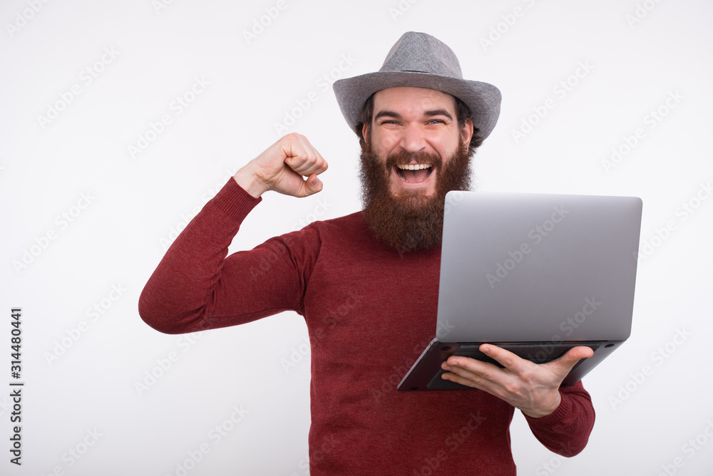 Happy young man celebrating and holding laptop