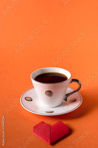 cup of coffee and heart made of paper on orange trendy background with space for text