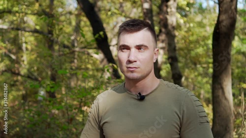 Portrait of a man on a background of green trees in a forest. The man looks disapprovingly and incredulously around, for fear of danger photo