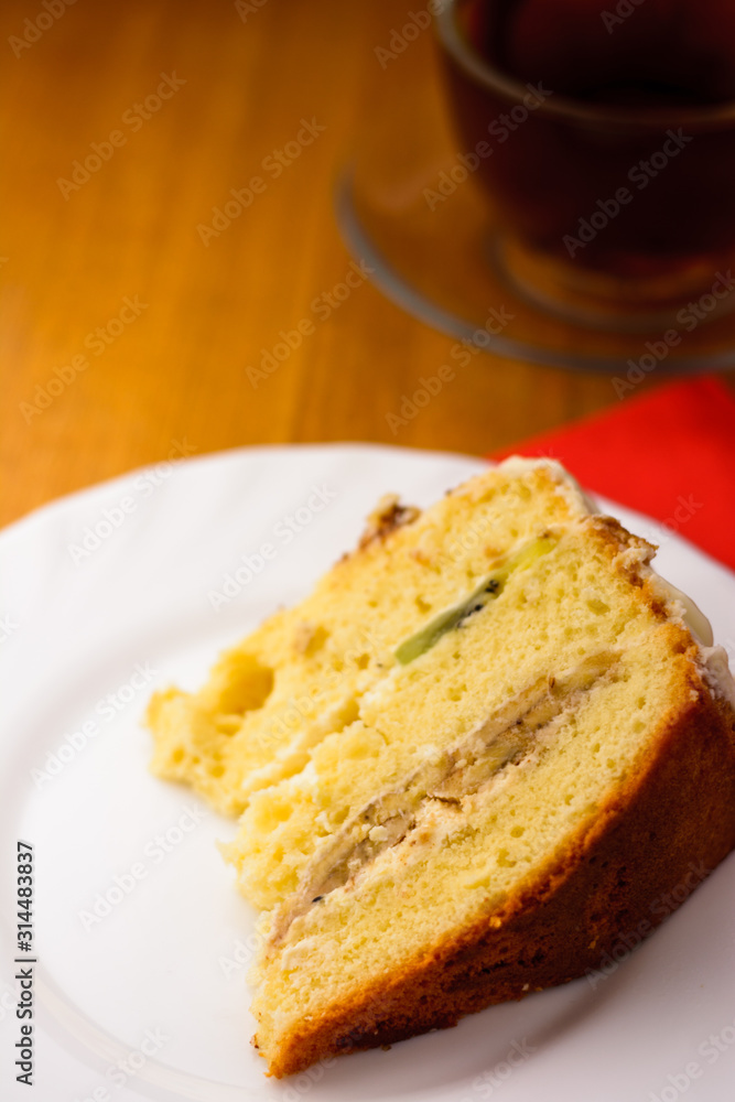 sponge cake on a white plate on a wooden background with a cup of black tea in a glass cup