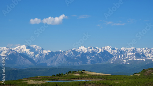 Small melt lake on a mountain plateau. Mountain oasis against the backdrop of a snowy ridge. Summer Altai.