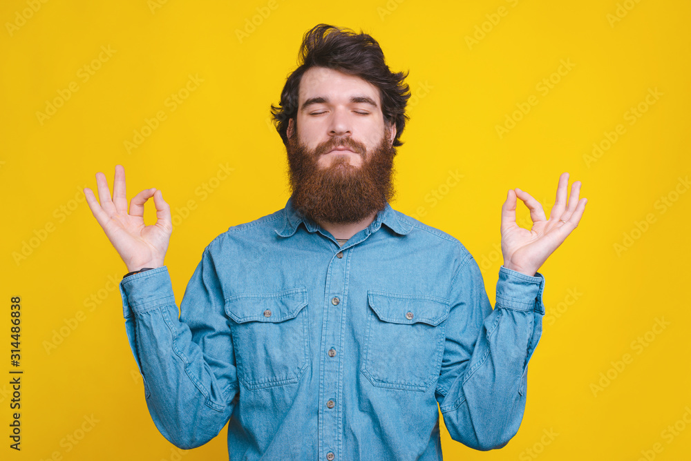 Photo of bearded hispter man in blue shirt doing meditation Photo of bearded hispter man in blue shirt doing meditation