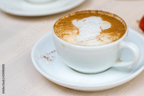 hold ceramic white with cappuccino above wooden plate and rustic table. Milk foam on top in heart shape