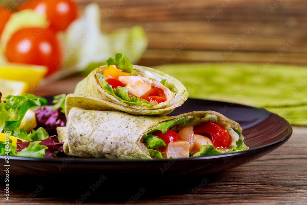 Spinach wrap with meat and vegetables on black plate with green salad. Spinach wrap with meat and vegetables on black plate with green salad.