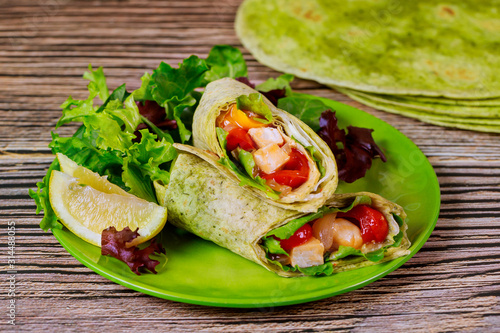 Wrap with grilled chicken and vegetable on plate with green salad and lemon.