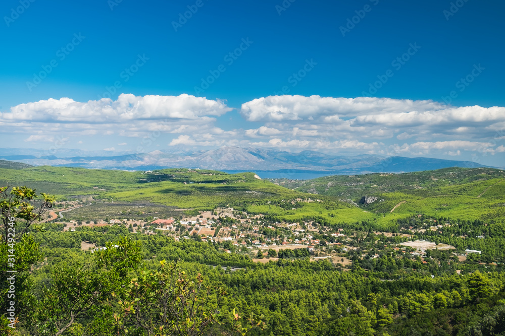 Typical natural rural landscape in East Attica in Greece. Green forest on hillsides and Malakasa village with red roofs, mountains and sea on the horizon