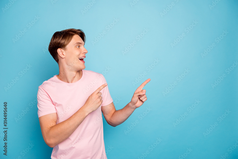 Photo of attractive excited guy indicating fingers empty space advising new shopping prices addicted shopper wear casual pink t-shirt isolated blue color background Photo of attractive excited guy indicating fingers empty space advising new shopping prices addicted shopper wear casual pink t-shirt isolated blue color background