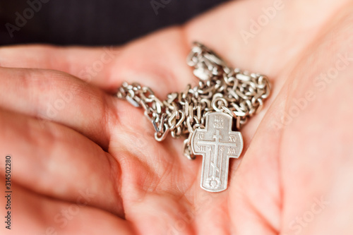 Silver cross in the hand with focus on the cross, shallow DOF