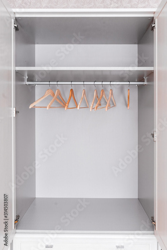 Home furniture. Spacious, bright and grey wardrobe from inside.Empty top drawer. Modern wooden clothes hangers hang on metal hook on rod