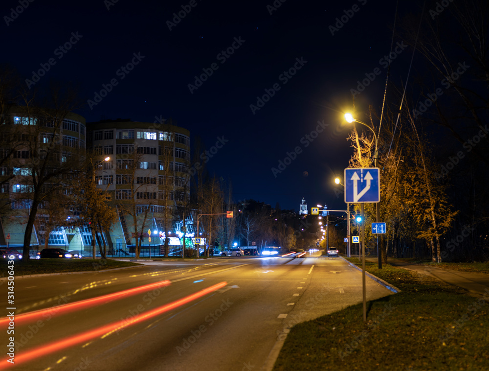 Street at night in a small town. Lights of lamps, shop windows and passing cars at a slow shutter speed.