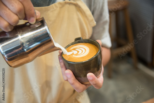 Barista pouring milk in to coffee cup making beautiful latte art.Coffee latte art in coffee shop