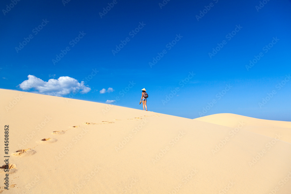 beautiful girl in the desert goes on a hill barefoot on the sand with a hat and shoes in her hands