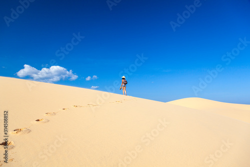 beautiful girl in the desert goes on a hill barefoot on the sand with a hat and shoes in her hands