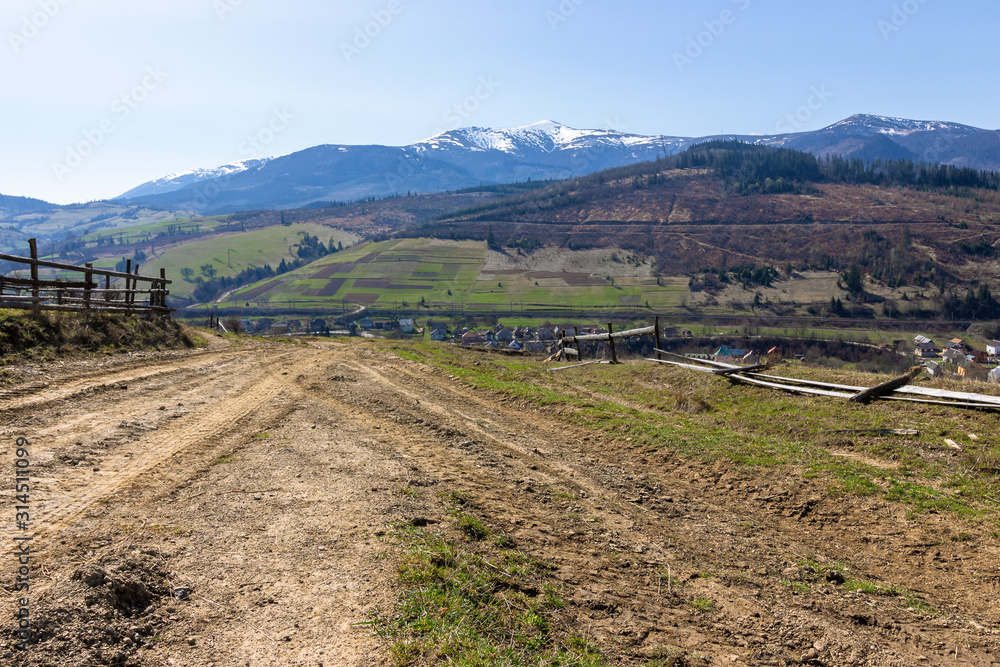 rural landscape in spring. mountain ridge in the distance with snow capped tops and fields with fence along the country dirt road. warm sunny weatherrural landscape in spring. mountain ridge in the di