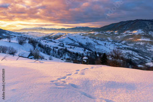 mountainous countryside in winter at sunrise. snow covered hills and fields of carpathian rural area rolling off in to the distant krasna ridge. glowing fog in the valley. colorful clouds on the sky