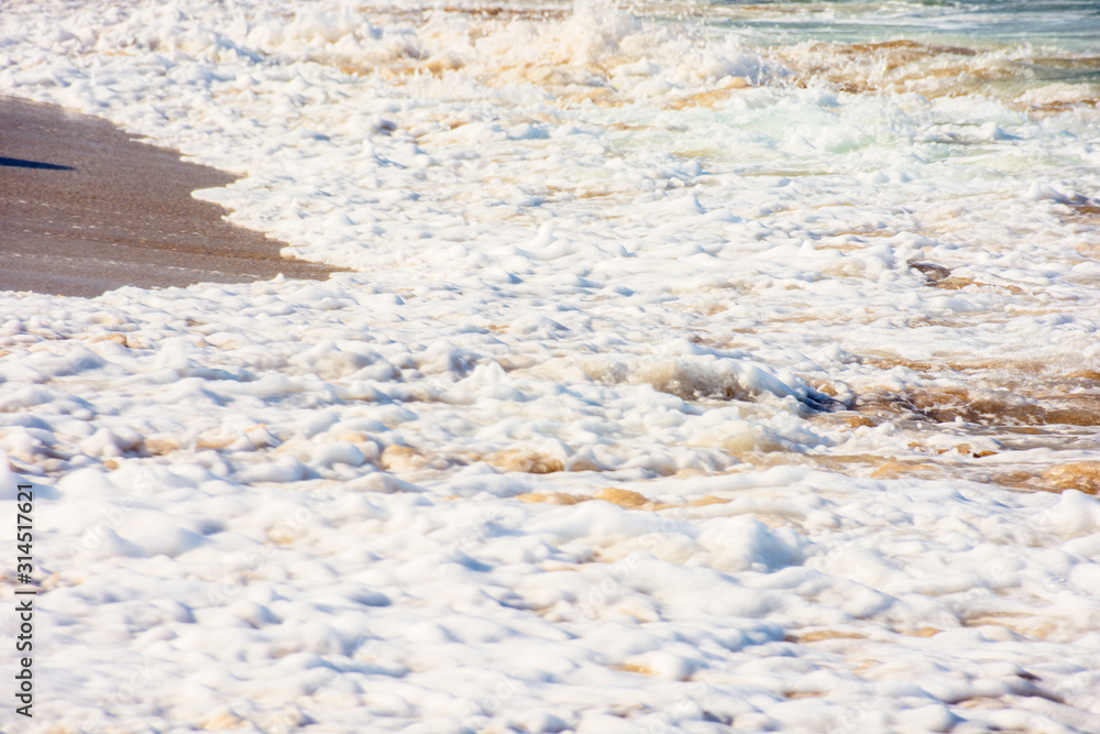 sea waves splash foam on the sunny beach. mess of salt water and sand in evening light. dynamic nature texture sea waves splash foam on the sunny beach. mess of salt water and sand in evening light. dynamic nature texture