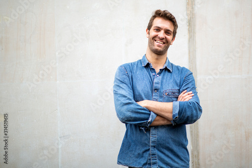 older guy smiling with arms crossed by white wall © mimagephotos