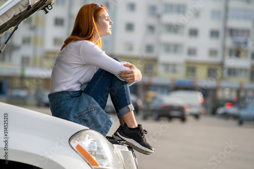 Young stressed woman driver near broken car with popped hood waiting for assistance. photo