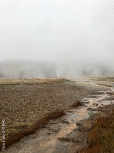 Nordic landscape in Haukadalur valley (Iceland) on a cold autumn / winter day in the geothermal area of The Great Geysir: mud roads, rocks & volcanic nature releasing hot water through geyser springs