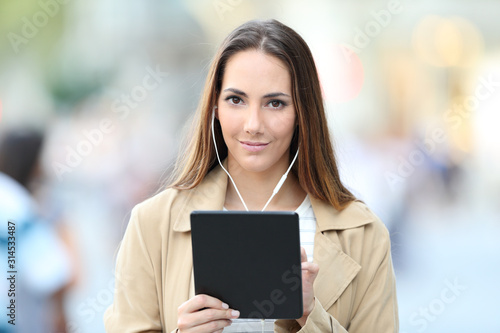 Serious girl wearing earbuds holds a tablet looking at you