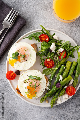 Toasts with asparagus and a fried egg on a white plate, top view, grey background.