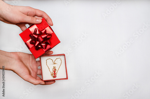 Jewelry as a gift for Valentine's Day. Holiday sale. Gold chain with red stones in the form of a heart in a box in the hands of a woman on a white background.