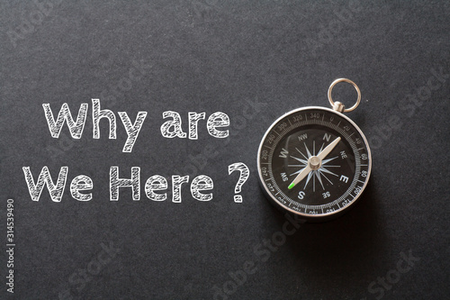Written Why are We Here? words on black background with compass