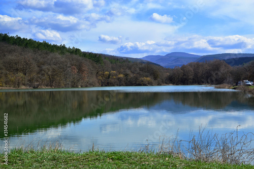 Beautiful lake, forest and mountains in early spring. Bashtanovka village, Crimea. A very beautiful spring landscape: forest, mountains, clouds. For cards, calendars, design.Spring forest