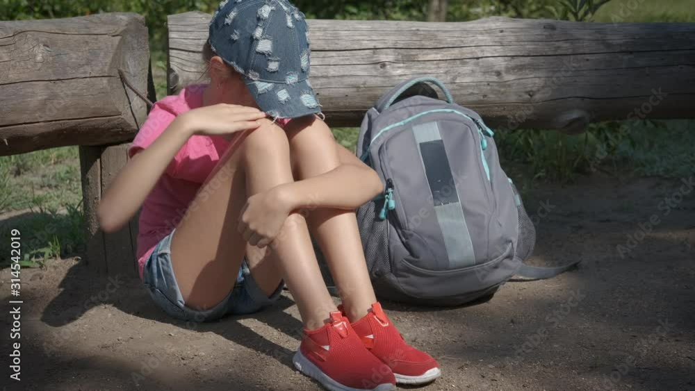 Lost child in the park. The offended schoolgirl sits on the ground in the park, next to her is a schoolbag. Lost child in the park. The offended schoolgirl sits on the ground in the park, next to her is a schoolbag.