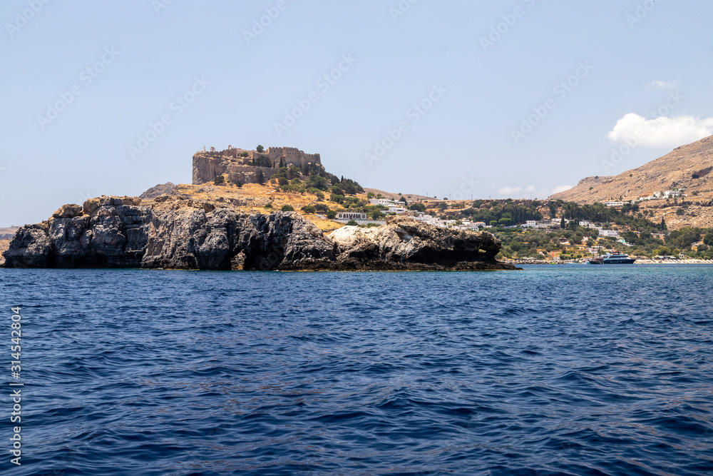 View from a motor boat on the mediterranean sea at the rocky coastline and the acropolis of Lindos on the eastside of Greek island Rhodes