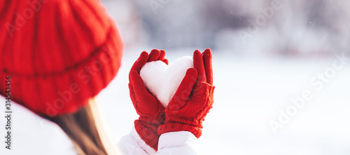 Woman in red gloves and hat holding heart shape from snow, Valentines day, sun set. love concept. photo