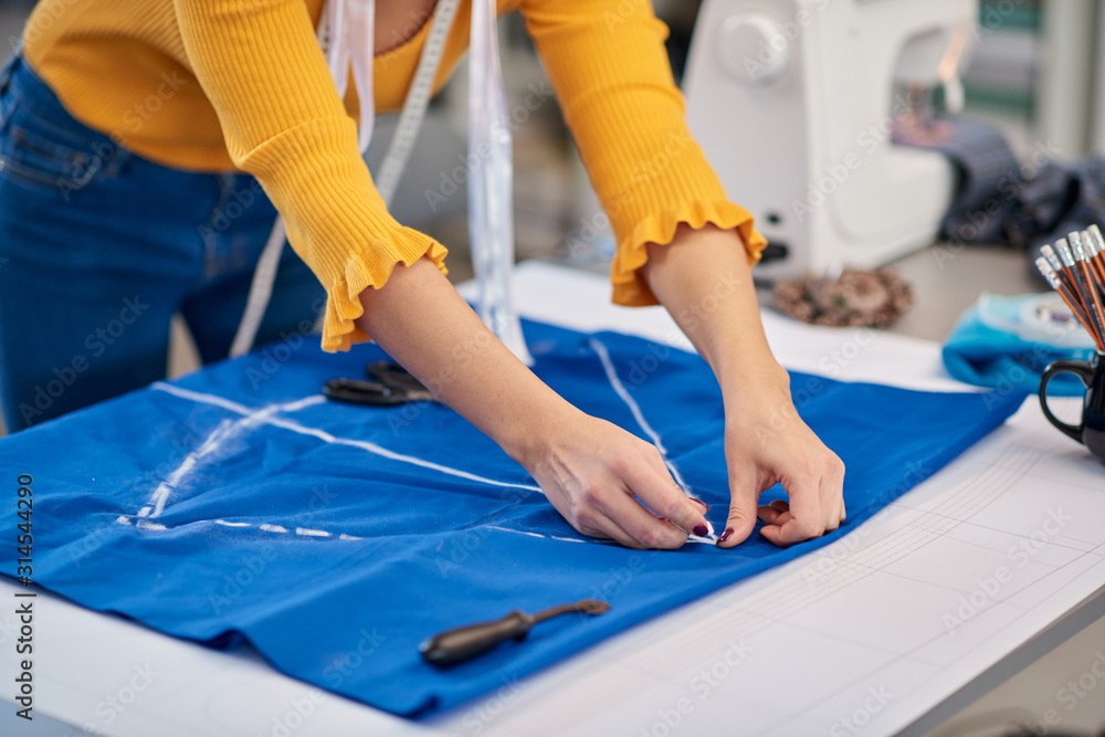 Creative caucasian fashion designer standing in her studio and drawing scheme on blue linen for a beautiful night dress. Creative caucasian fashion designer standing in her studio and drawing scheme on blue linen for a beautiful night dress.
