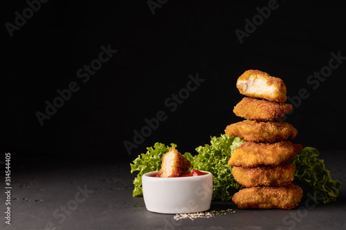 Cooked chicken nuggets in breadcrumbs with lettuce and a bowl of ketchup on a dark background with place for text photo