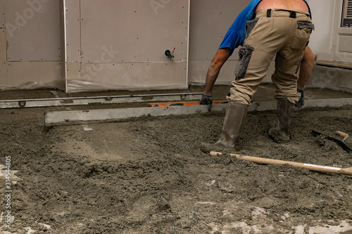 Floor screed is processed in the apartment. The worker performs a sand-cement floor screed.