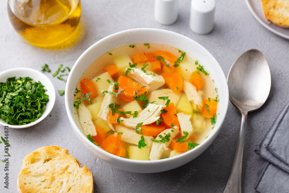 Chicken soup with vegetables in white bowl. Grey stone background. Close up. Chicken soup with vegetables in white bowl. Grey stone background. Close up.