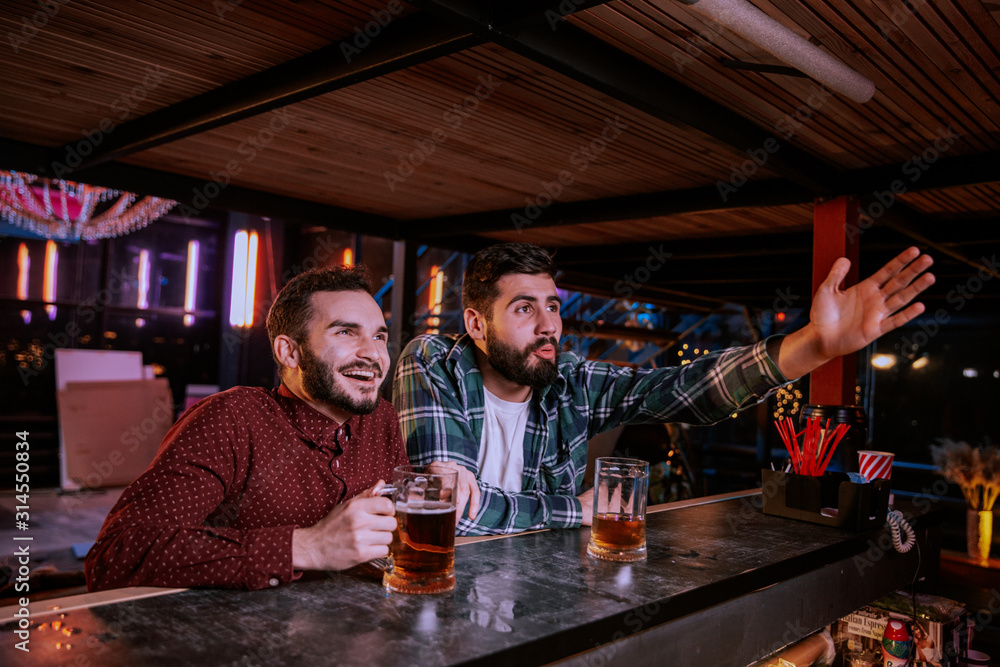 Two buddies drinking beer and watching sport competition in pub, leisure Two buddies drinking beer and watching sport competition in pub, leisure