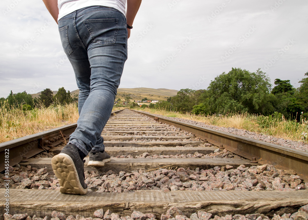 Unrecognizable young man walking on the railway tracks in a rural scene in a cloudy day Unrecognizable young man walking on the railway tracks in a rural scene in a cloudy day