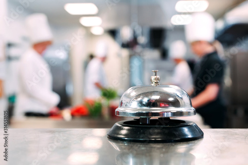Table distribution in the restaurant. Cooks prepare food in the kitchen against the background of a metal bell. © davit85