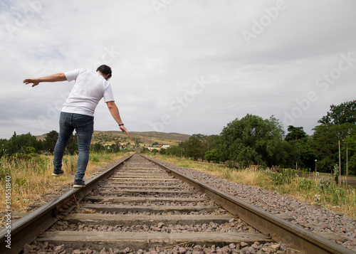 Unrecognizable young man balancing on the railway tracks in a rural scene in a cloudy day