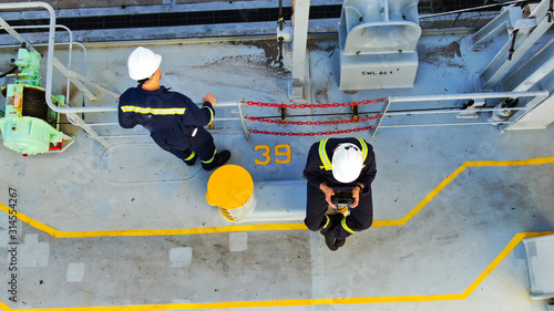 Two seaman on deck of container ship wearing boiler suit and helmets.
