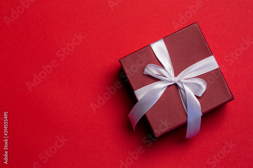 Red gift box with a white ribbon on red background, Valentine's Day concept, top view, copy space