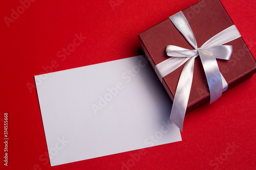 Blank paper and giftbox on red background, top view, Valentine's greetings card, copy space
