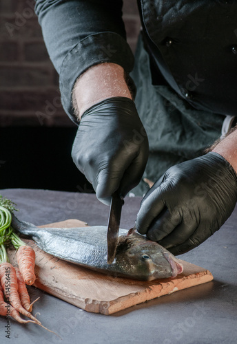 cleaning a fish with a knife on a wooden surface. hands in black gloves