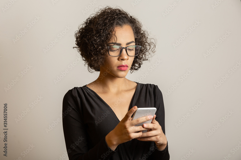 Front portrait of smiling young african american woman looking at cellphone with glasses. Beautiful young girl with curly hair using her smartphone to chat with friends. connected concept Front portrait of smiling young african american woman looking at cellphone with glasses. Beautiful young girl with curly hair using her smartphone to chat with friends. connected concept