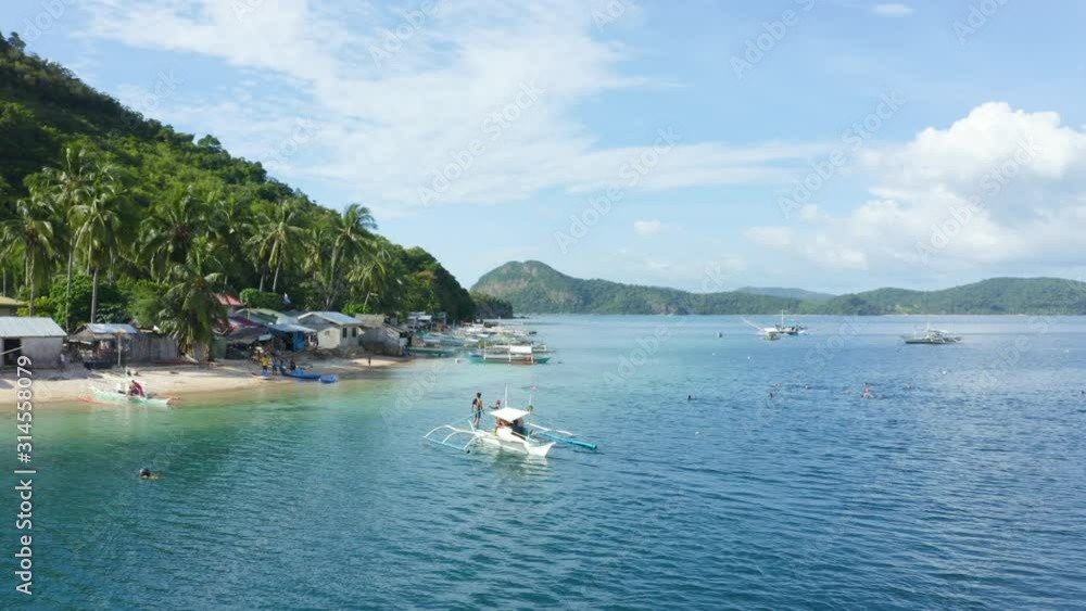 Aerial orbit of a typical Philippine fishing boat on the sea with a tourist beach and swimmers enjoying the clear Pacific ocean Aerial orbit of a typical Philippine fishing boat on the sea with a tourist beach and swimmers enjoying the clear Pacific ocean