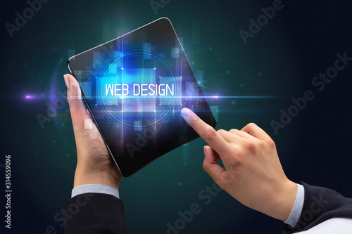 Businessman holding a foldable smartphone with WEB DESIGN inscription, new technology concept