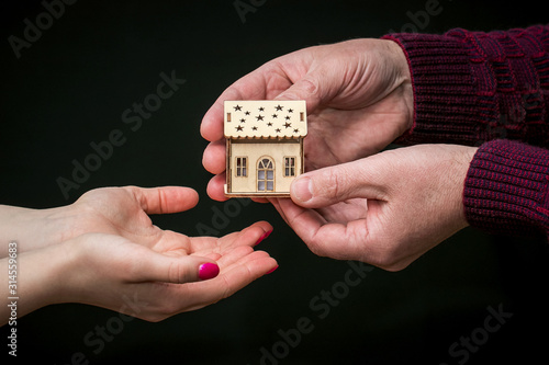 Man hands woman a wooden toy house_ © Volodymyr