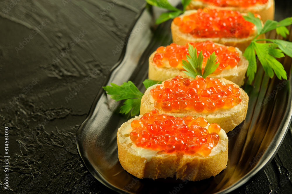 Slices of fresh white bread with red caviar and parsley on the black dish, on the black background. Slices of fresh white bread with red caviar and parsley on the black dish, on the black background.